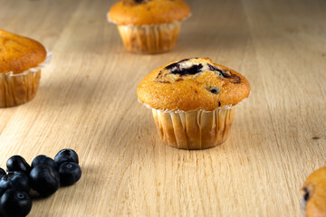 A blueberry muffin sits on a wooden table next to a few blueberries. The muffin is the main focus of the image, and the blueberries are a complementary element. Concept of freshness and simplicity