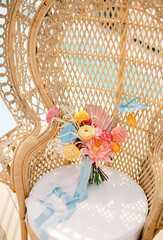 Colorful bridal bouquet stands on a white cushion of a beige wicker chair