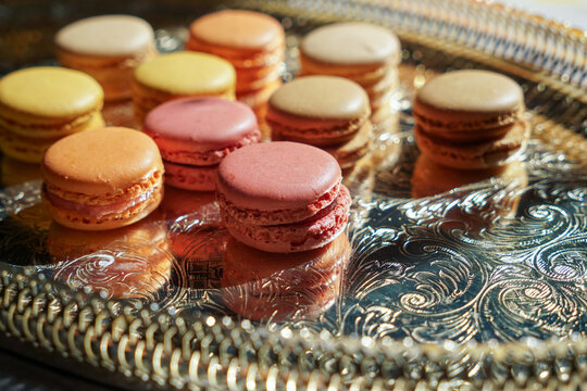 Macaroons of different colors with different flavors and pearl beads on the golden metal tray. Sweet treats for guests to the wedding or party. - Powered by Adobe