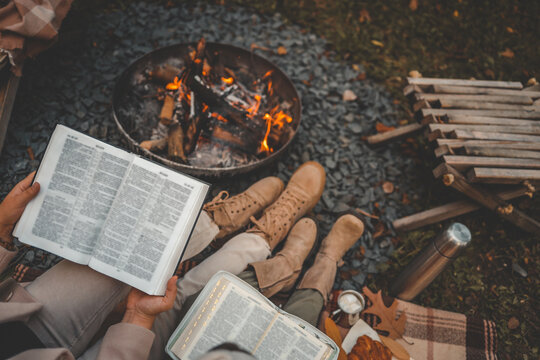 Mother and child reading the Bible together by a cozy autumn campfire with hot cocoa and croissants on a blanket