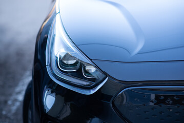 Close-up of a modern car headlight with a sleek, reflective surface. Luxury vehicle front detail with glossy black paint and LED design.