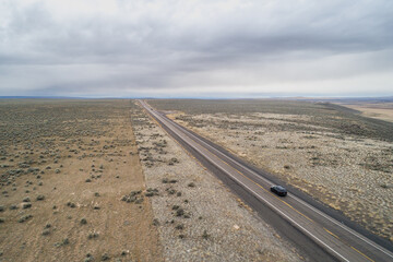 A car is driving down a long, empty road in a desert