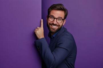 Cheerful businessman playfully peeking from behind a purple wall, engaging with the camera