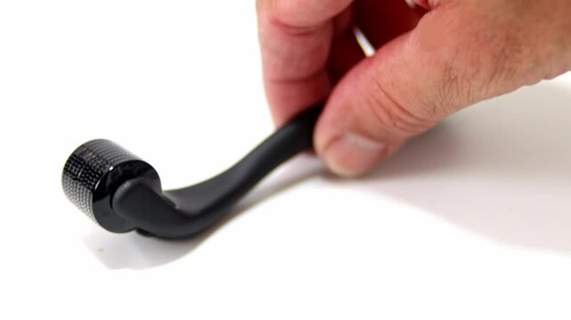 A hand holding a black microneedle roller for skincare and facial rejuvenation. Professional derma roller tool for beauty treatments, collagen stimulation, and anti-aging therapy.