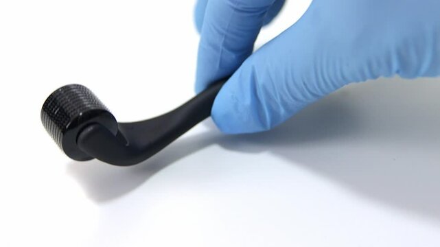 A hand with latex gloves holding a Black microneedle roller for skincare and facial rejuvenation. Professional derma roller tool for beauty treatments, collagen stimulation, and anti-aging therapy.