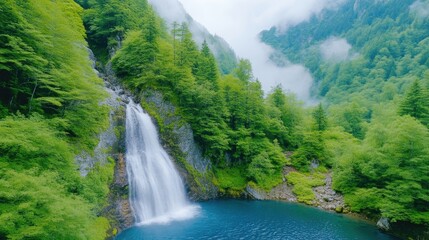 Fototapeta premium Lush waterfall cascading into a vibrant blue pool, surrounded by dense green forest and misty mountains