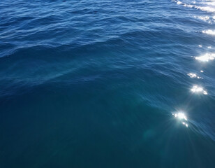 Fototapeta premium Ocean water surface with gentle waves, deep blue tones, sunlight shimmering on the surface, high-detail photography
