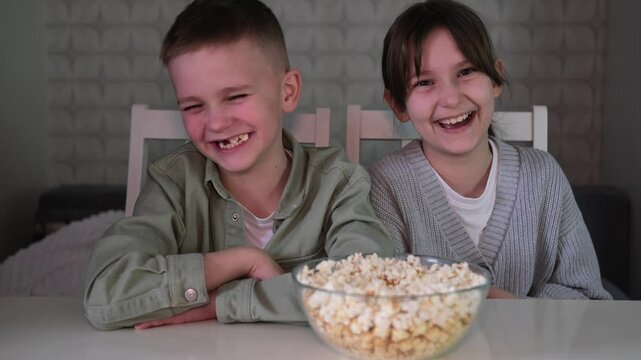 ute happy children are smiling happily. Brother and sister are sitting and watching cartoons or movies, eating popcorn. Lifestyle. Concept of human emotions.	
