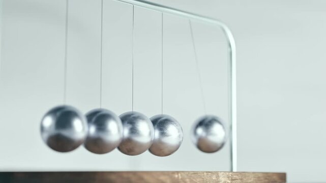 Close-up view of smooth motion of metallic balls in Newton's cradle. Kinetic pendulum. Focus blur, light backround. Seamless looped 4k 3d animation. Popular physics experiment demonstration slowed.