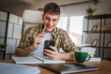 young man student study for exam from notes and mobile phone at home