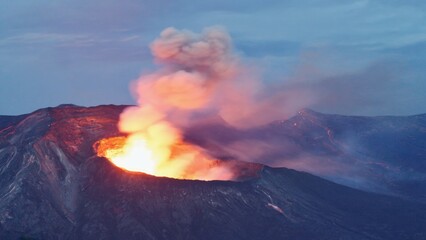 Fototapeta premium A large plume of smoke rises from the top of a mountain, with clouds and trees in the background