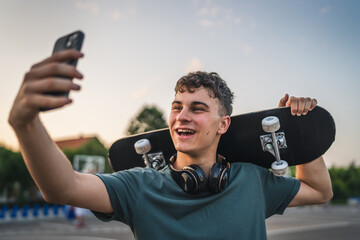 One man young adult caucasian teenager stand outdoor with skateboard on his shoulder and headphones posing at basketball court portrait happy confident wear shirt casual real person copy space