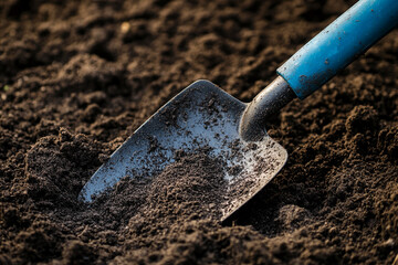 Close-up of a small shovel in dark soil, showcasing texture and detail of gardening tool and earth, representing spring planting and growth