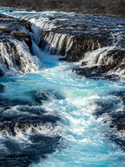 Bruarafoss Waterfall in Iceland: Crystal-clear, vibrant turquoise water cascades over basalt rocks in a stunning winter landscape. Nature's pure beauty