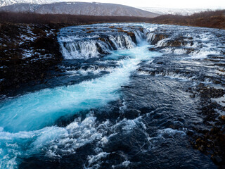 Bruarafoss Waterfall, Iceland: Turquoise waters cascade over dark volcanic rocks, creating a vivid contrast. A scenic and iconic natural landmark in the Icelandic wilderness