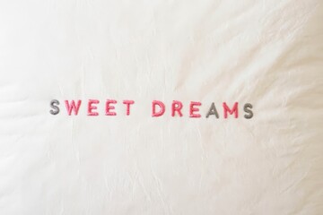 White pillow with embroidered 'Sweet Dreams' text in pastel colors.