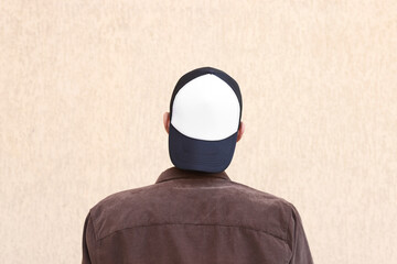 Man in stylish baseball cap near beige wall, back view. Mockup for design