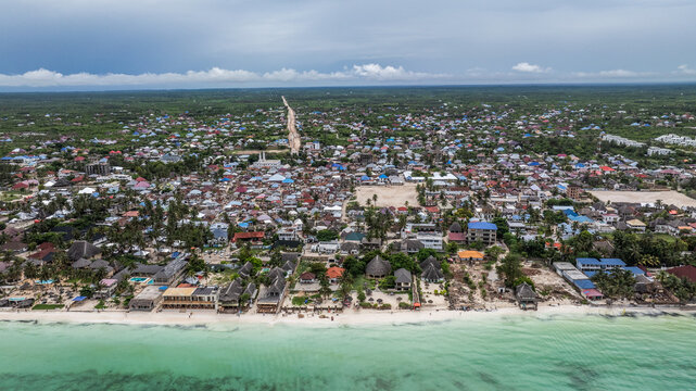 aerial landscape view of coastline with white sand beach in front of Downtown Paje, located on  island of Unguja, part of Zanzibar in Tanzania,  with countryside landscape in background 