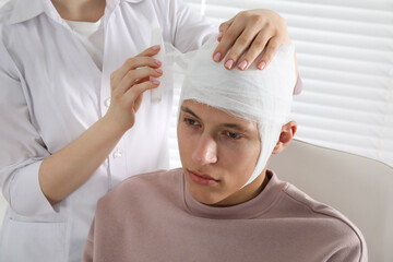 Doctor bandaging patient's head in clinic, closeup