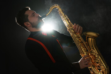 Professional musician playing saxophone on black background with smoke