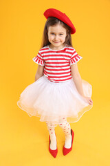Stylish little girl wearing oversized high heeled shoes on orange background