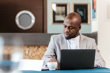 Focused serious african american businessman accountant analyst holding documents looking at laptop...