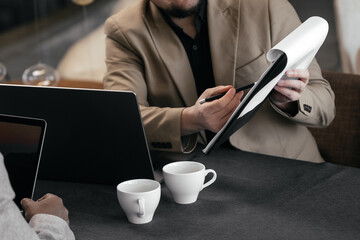 Cropped shot of business professionals discussing financial marketing data while sitting at a table with project documents during a business lunch and cup of tea, coffee.