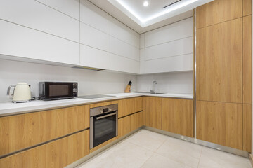 Modern kitchen interior design. The kitchen set is decorated with white and wooden panels. Stylish household appliances.