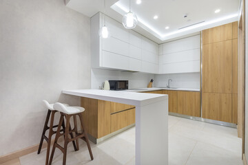Kitchen design with modern interior. Kitchen set made of light wood with white elements. High bar stools at the white table.