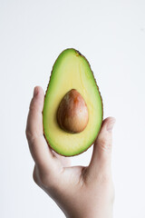 Hand holding fresh half avocado with seed on white background
