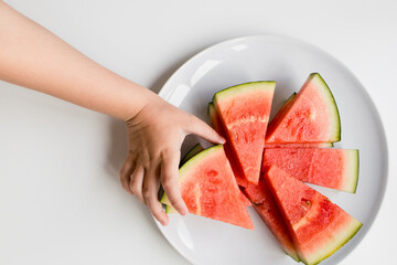 Child hand reaching for sliced watermelon on white plate
