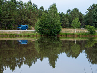 Vistas de una furgoneta azul reflejada en el Étang du Petit Broustier  en Laruscade, Francia. Con paisaje verde de árboles, en Francia verano de 2022