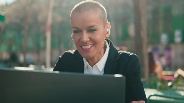 Businesswoman having a video meeting using her laptop at a table in a plaza. She looks professional and happy.