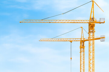 Two yellow construction cranes against a clear blue sky