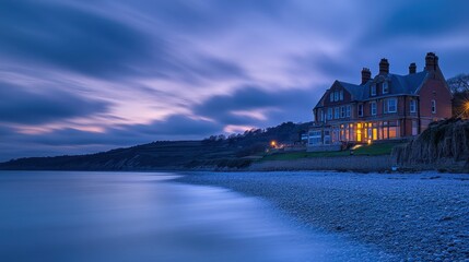 Fototapeta premium Seaside house at dusk with long exposure cloudy sky and pebble beach. Use for travel, vacation or real estate advertisements and websites.