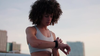 Woman Checks Fitness Tracker on Rooftop at Sunset - Powered by Adobe