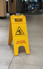 Bright Yellow Caution Warning Sign Indicating Slippery Conditions in Modern Indoor Space. A yellow...