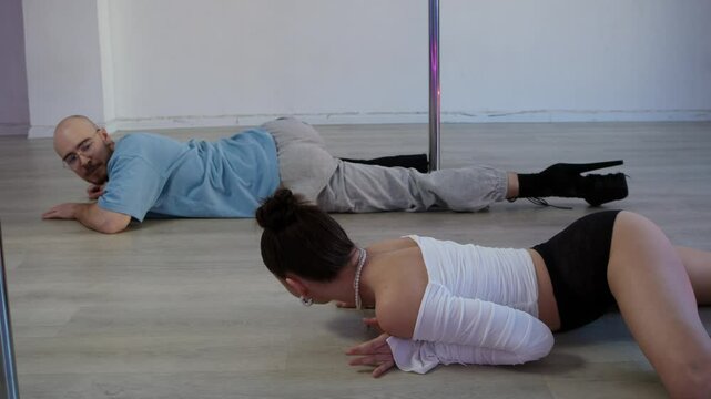 A young woman shows booty movements by teaching a stern man seductive dancing