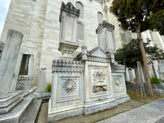Ornate stone carvings on mosque exterior wall surrounded by garden with leafy trees Delicate...