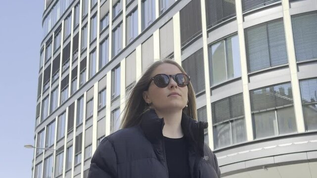 Tourist enjoying sunny day in front of austrian parliament building. Cheerful redhead woman wearing sunglasses relaxing outdoors, gazing upward with austrian parliament building under bright sky