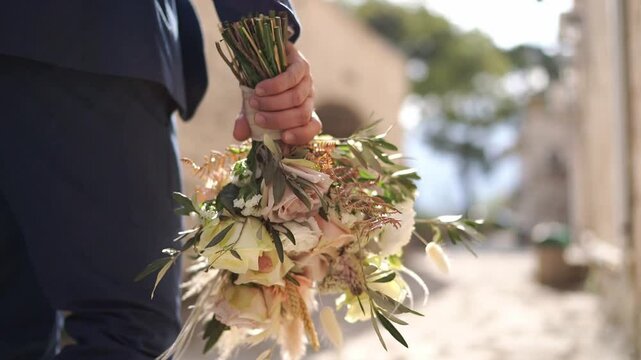 Bouquet of flowers in the groom hand, walking down the street. Cropped