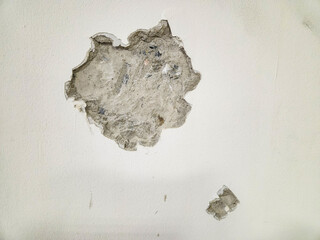 Wall damage, large crack and smaller hole in the surface of a white wall.