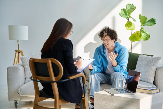 Young smiling male patient in mental therapy talking to psychotherapist, counsellor