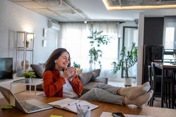 Happy freelancer woman drinking coffee working from home office