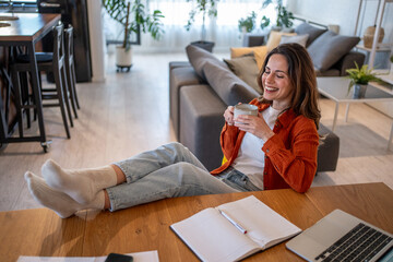 Freelancer enjoying a coffee break with feet up on desk at home
