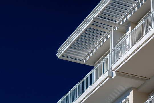 The white metal roof of an apartment building is seen from a distance, set against a vibrant deep blue sky, showcasing modern architecture and clean lines.