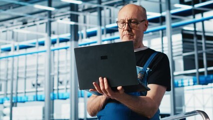 Elderly engineer uses laptop in smart factory to test automated systems, ensuring reliability. Experienced technician uses notebook to identify bottlenecks and optimize equipment, camera A