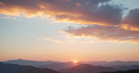 Obraz premium Beautiful landscape featuring a mountain range at sunset with sun partially visible at the horizon, casting a warm, orange glow across the sky.