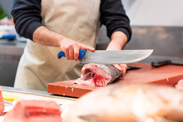 A fishmonger skillfully fillets a fresh fish with a large knife at a seafood market. The scene captures the essence of fresh, healthy, and protein-rich seafood, perfect for summer meals.