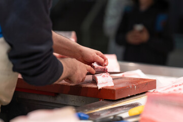 A fishmonger skillfully fillets a fresh fish with a large knife at a seafood market. The scene...